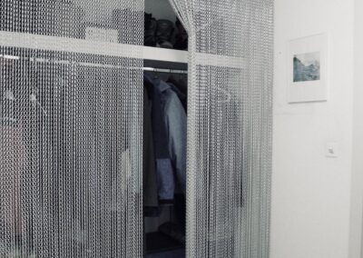 Der krismar Fliegenvorhang montiert als Sichtschutz vor einer Garderobe anstelle von verschlossenen Schranktüren. Aufgrund der Massanfertigung und des schlichten Designs kann der Vorhang auch als innenarchitektonisches Element verwendet werden.